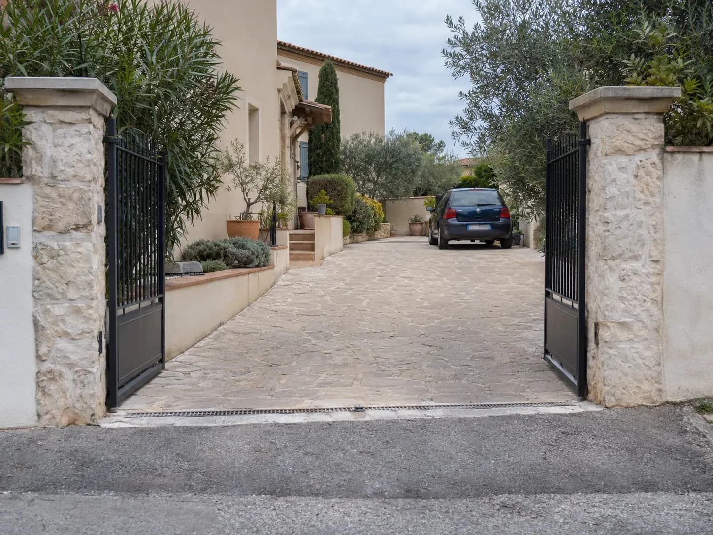 Allée d'une propriété vue depuis la rue, portail ouvert, voiture garée au fond